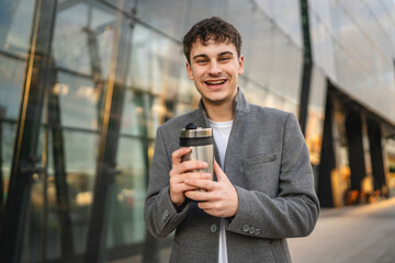 portrait of young man stand with thermos in front modern building