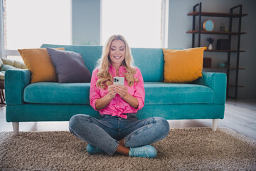 Young woman enjoying leisure time on phone in bright living room with colorful decor, smiling and engaging with content