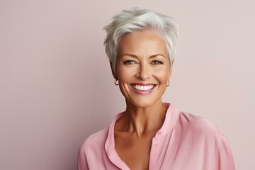 Fototapeta premium Portrait of a beautiful senior woman with short grey hair smiling on a pink background, showing perfect teeth