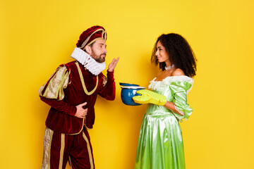 Fototapeta premium Couple in Retro Costumes on Yellow Background Portraying Aristocratic Era and Modern Life