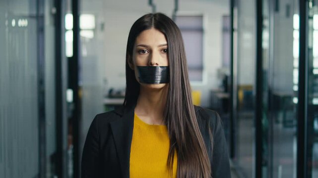 Young woman in a professional setting with her mouth taped shut, removing the tape and smiling confidently. Concept of empowerment, overcoming challenges, and personal expression