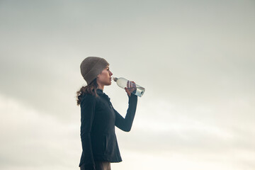 woman drinking from a water bottle outdoors while exercising