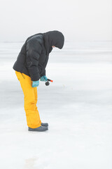 Winter fishing. A fisherman with a fishing rod tries to catch a fish in a frozen river. 