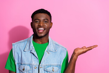 Portrait of a young, stylish man in a denim vest enthusiastically gesturing with open palm against...