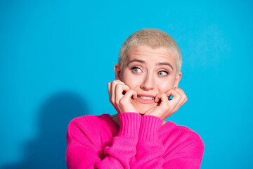 Young woman with short blond hair wearing a pink pullover against a vibrant blue background