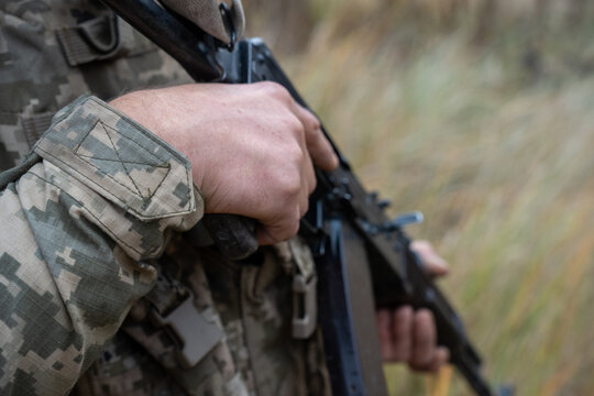 Close-up of a Ukrainian soldier's hand gripping a rifle. The image highlights the soldier's firm grasp and the texture of the camouflage uniform, showing readiness for action.