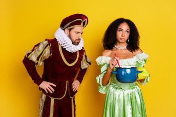 Couple in noble retro costumes standing with a cooking pot on a bright yellow background, blending historical elegance