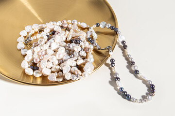 Pearl threads or necklaces on golden tray on white background. Various natural pearl beads