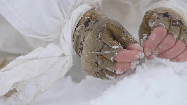 Sapper soldier places an anti-personnel mine on a tripwire. Military sapper mines and camouflages a mine in snow. Soldier in a winter camouflage suit mines an area. Preventing enemy entering area