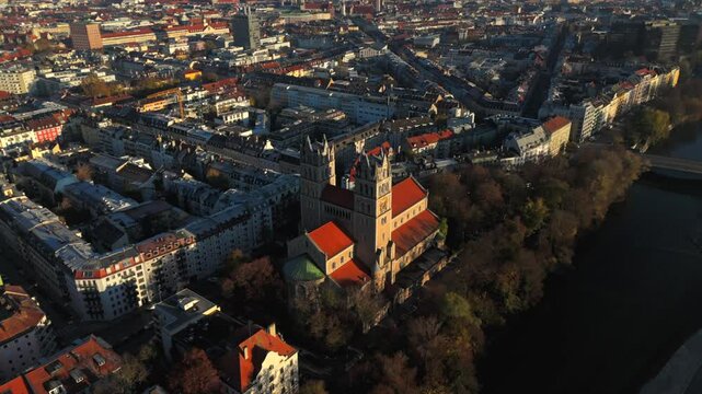 Kath. Pfarramt St. Maximilian Katholische Kirche in Munchen, Bayern, Deutschland Luftaufnahme. Aerial view of St. Maximilian in Munich with distinctive towers at sunrise, surrounded by autumn colors. 