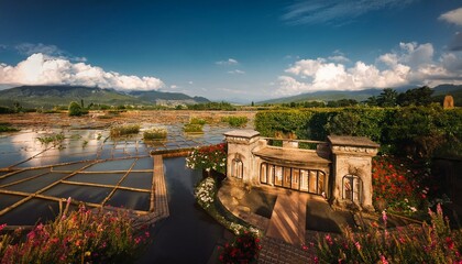 Naklejka premium Serene landscape with a quaint building overlooking a water feature and mountain backdrop.