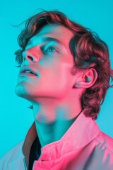 Fototapeta premium A confident man gazes upward against a vibrant neon pink and blue background, highlighting his facial features and stylish jacket