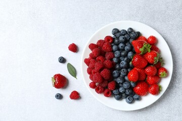 Different fresh ripe berries in bowl on gray table