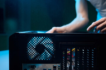 A man cleans a computer case with a vacuum in a bright room, stressing workspace tidiness