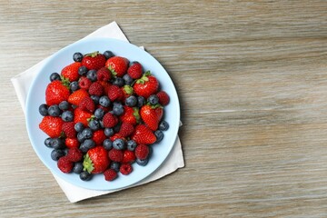 Different fresh ripe berries in bowl on wooden table, top view