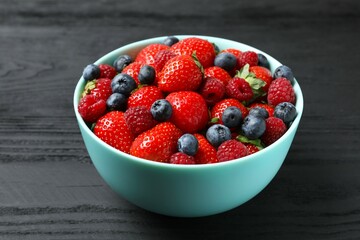 Different fresh ripe berries in bowl on wooden table