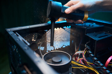 A man cleans a computer case with a vacuum in a bright room, stressing workspace tidiness