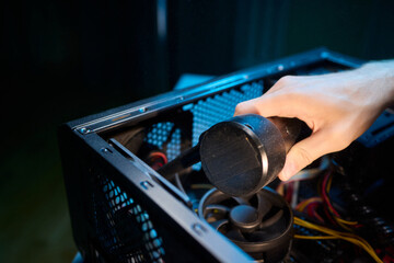 A man cleans a computer case with a vacuum in a bright room, stressing workspace tidiness