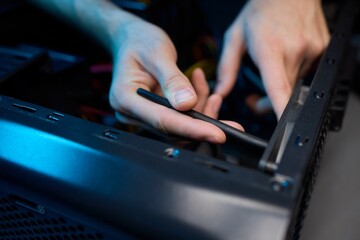 A man cleans a computer case with a vacuum in a bright room, stressing workspace tidiness