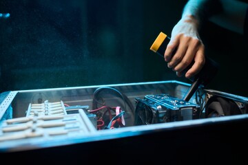 A man cleans a computer case with a vacuum in a bright room, stressing workspace tidiness