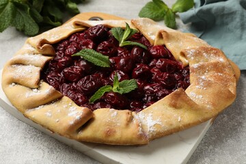Tasty galette with cherries and mint on light table, closeup