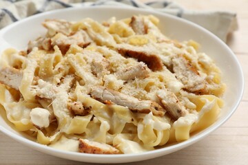 Tasty Alfredo pasta with chicken on light wooden table, closeup