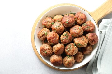 Tasty cooked meatballs with green onion in bowl on white table, top view. Space for text