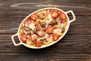 Delicious pasta casserole with cheese, tomatoes and minced meat in baking dish on wooden table, top view