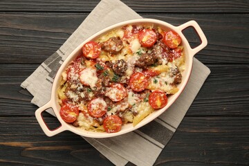 Delicious pasta casserole with cheese, tomatoes and minced meat in baking dish on wooden table, top view