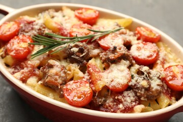 Delicious pasta casserole with cheese, tomatoes, minced meat and rosemary in baking dish on grey table, closeup