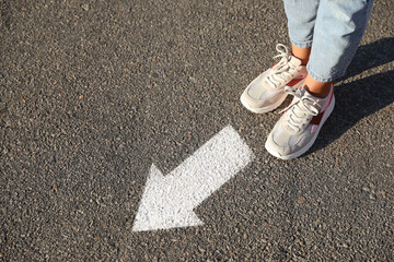 Woman walking toward white arrow on asphalt road, closeup. Move forward