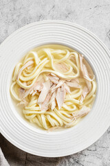 chicken noodle soup with herbs in a white bowl