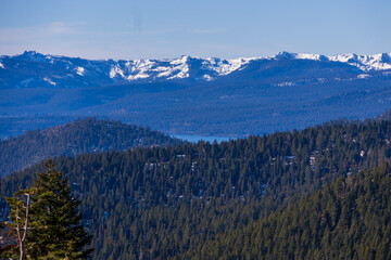 a stunning shot of the vast clear blue lake water with snow capped mountain ranges and lush green trees along the banks of the lake and blue sky at Lake Tahoe Nevada State Park in Incline Village.