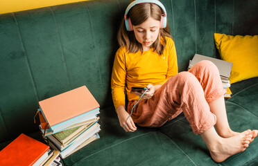 Smiling little caucasian girl in headphones have video call or distant class using her...