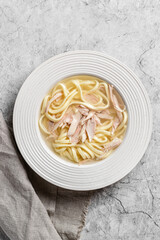 chicken noodle soup with herbs in a white bowl