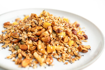 A bowl of granola with nuts and seeds on a white plate. The granola is a mix of different types of grains and nuts, and it looks like a healthy snack.