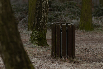 In a serene forest clearing surrounded by tall and lush trees, there stands a wooden trash bin, promoting cleanliness and environmental care