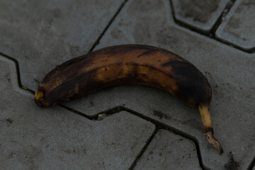 A neglected, discarded banana rests on a paved outdoor surface, drawing attention to the issues of urban waste and environmental challenges