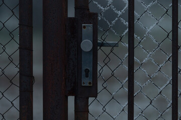 A metal latch is attached to a gate that is situated within a chain link fence, and the entire...