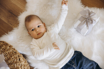 Baby lying on white fur carpet looking up near a gift