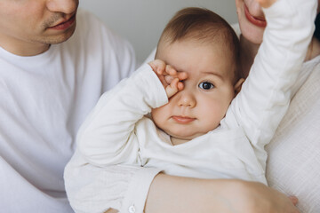 Sleepy baby rubbing eyes while being held by parents