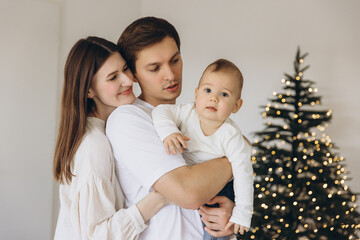 Young family holding their baby near Christmas tree