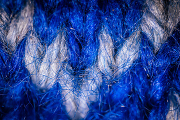 Obraz premium A detailed macro shot of blue and white knitted fabric, showcasing the soft texture and intricate weave of the yarn. The color contrast highlights the artistic pattern.