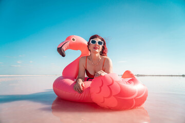 Woman, Flamingo Float, Pink Lake: A woman in sunglasses relaxes on a flamingo float in a pink lake...