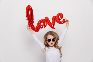 Little fashion stylish girl in white dress and sunglasses raising red word LOVE made of air...