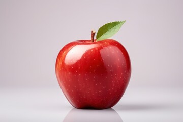 Fresh red apple on a clean surface with a vibrant green leaf during bright lighting
