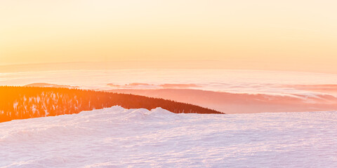 Eastern Sudetes, view of mountain range with thick fog in valley from peak from hiking trail during winter hike in mountains, viewpoint of wide winter landscape in mountains at orange sunset.