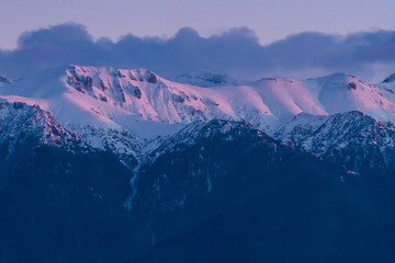 The Ridge of the Bucegi Mountains (Romania) Covered by Dark Clouds and Caressed by the Last Rays of Sun in Mid-Winter 