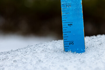 Ruler in snow measuring snowfall depth and ice accumulation from winter snowstorm.