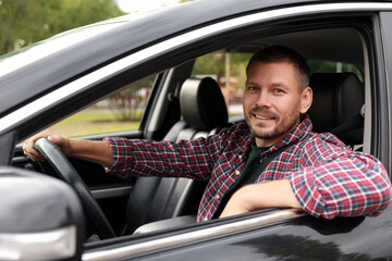 Happy man behind steering wheel of modern car, view from outside